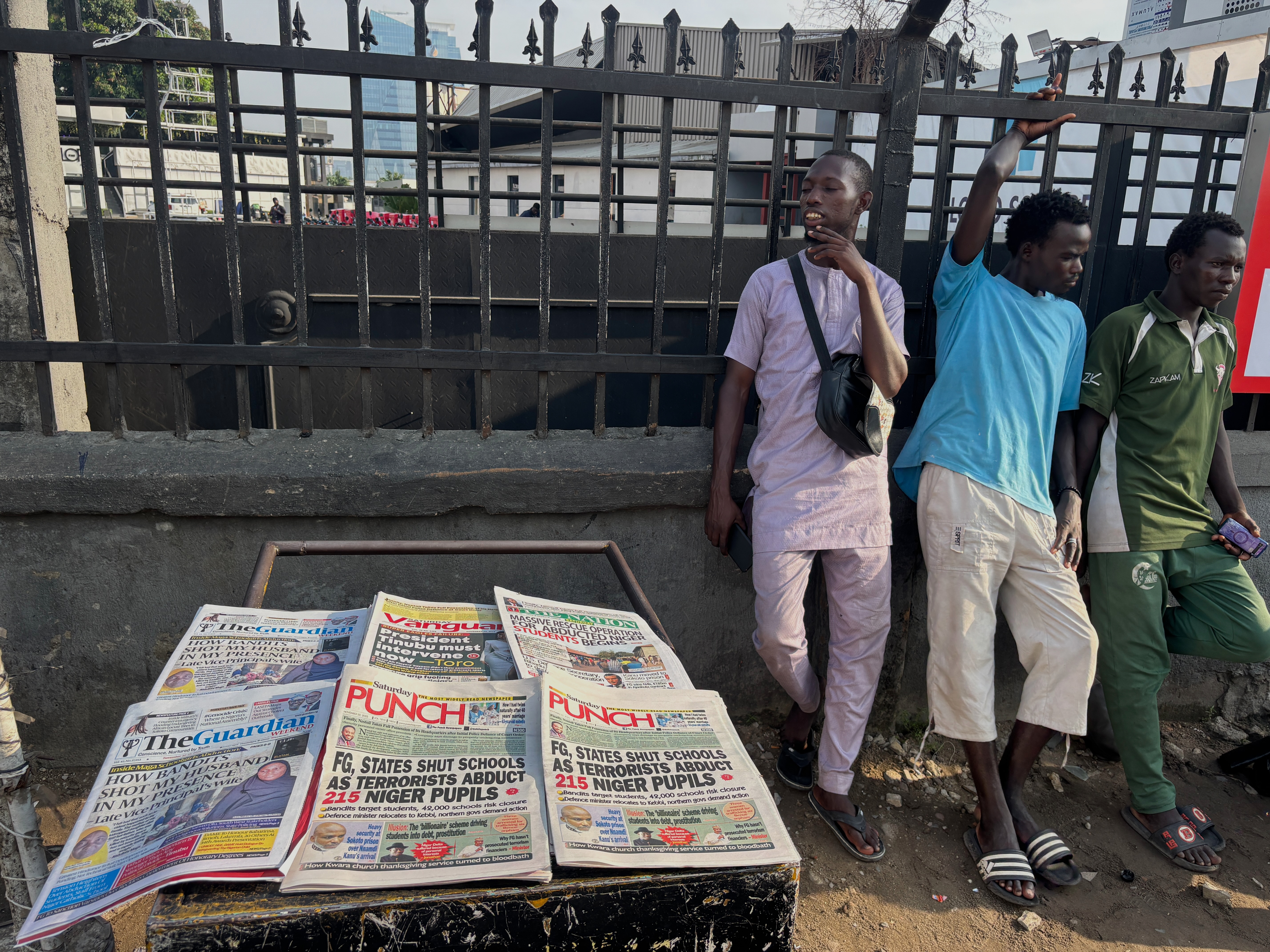 People stand near a display local newspapers on the street of Lagos with headlines on gunmen abducting schoolchildren and staff of the St. Mary
